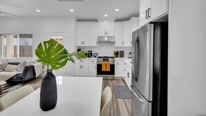 Une cuisine moderne avec des meubles blancs, un réfrigérateur en acier inoxydable et un coin repas comprenant une table et des chaises blanches.