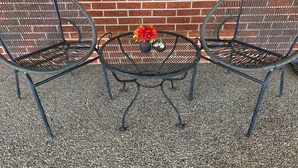 Two metal chairs and a small round table with a flower vase.