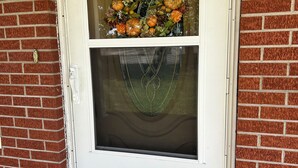 A white door with a glass panel above it, a brick wall, and a doormat with a leaf design.