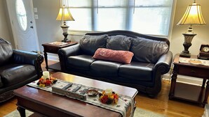 A living room with a dark leather sofa, a matching armchair, a wooden coffee table with decorative items, and two lamps on side tables.