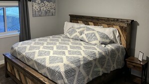 Una camera da letto con un letto in legno, una ventola a soffitto, una finestra con tende e un'opera d'arte appesa al muro.