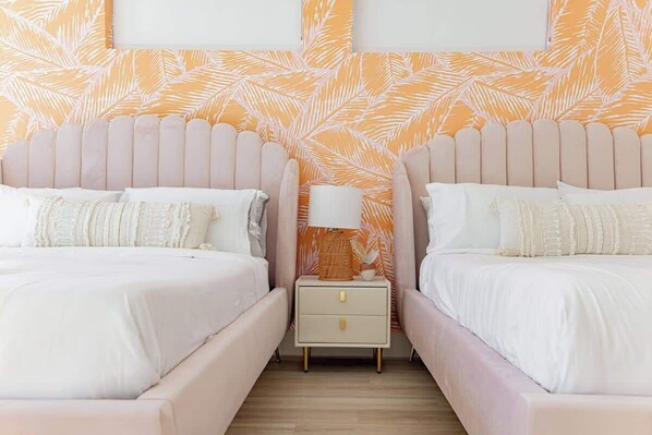 A double room with two beds, a nightstand with a lamp, and a patterned wall.