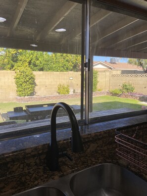 Enjoy a kitchen with a stainless steel sink, black faucet, and granite countertop, offering a view of the backyard with a deck and lush greenery.