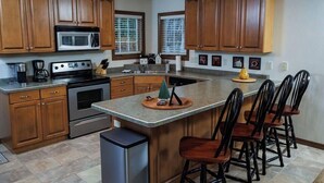 A kitchen with wooden cabinets, a microwave, stove, and a large island with bar stools. - Birch Grove Cottage, Downtown Fish Creek (Fish Creek)