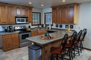 A kitchen with wooden cabinets, a microwave, stove, and a large island with bar stools.
