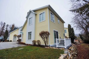 A two-story house with a front porch, a stone retaining wall, and a driveway. - Birch Grove Cottage, Downtown Fish Creek (Fish Creek)
