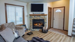 A living room with a stone fireplace, a flat-screen TV, a sofa, and a door. - Birch Grove Cottage, Downtown Fish Creek (Fish Creek)