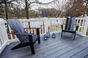 A deck with two Adirondack chairs, a white railing, and three blue lanterns.