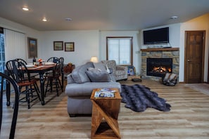A living room with a fireplace, a sofa, a dining table with chairs, and a television mounted above the fireplace.
