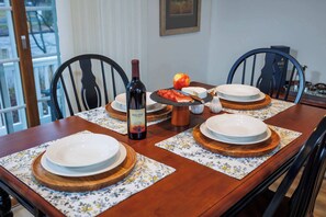 A dining table set with plates, a bottle of wine, and a fruit. - Birch Grove Cottage, Downtown Fish Creek (Fish Creek)