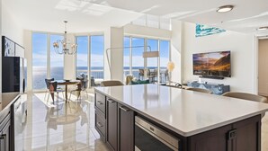 A modern kitchen with a large island, a dining area with a view, and a living space with a TV and artwork. - Gorgeous 3 BR Penthouse at Silver Beach (Destin)