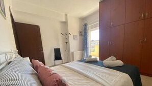 A hotel room with two beds, a wardrobe, a coat rack, and a window with curtains. - Impeccable Apt sleeps 5 in Heraklion (Heraklion)