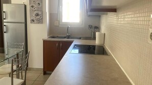 A kitchen with a stainless steel refrigerator, a glass dining table with metal chairs, a built-in stove, and a window with natural light. - Impeccable Apt sleeps 5 in Heraklion (Heraklion)
