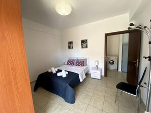 A bedroom with a bed, bedside tables, a chair, a wardrobe, and a washing machine.