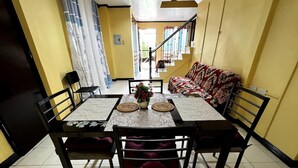 A dining area with a table set for four, surrounded by chairs. A sofa is visible in the background.