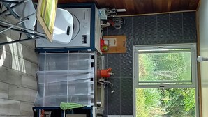 A compact kitchen with a wooden ceiling, a window with a view of greenery, a microwave, and a small refrigerator. - Poto Mitan (Tonate-Macouria)