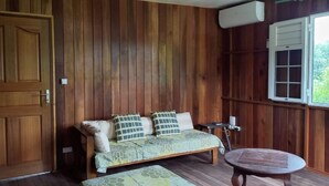 A wooden room with a sofa, a round table, and a window. - Poto Mitan (Tonate-Macouria)