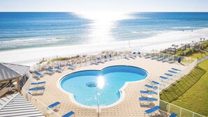 Une piscine en forme de cœur, entourée de chaises longues, avec vue sur une plage et l’océan.