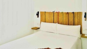 Una cama con sábanas blancas, una mesita de noche de madera y una lámpara de pared.