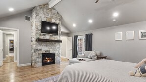 Un dormitorio con chimenea de piedra, una cama grande, un televisor montado en la pared y vistas al salón.