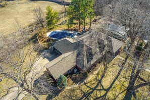 Vue aérienne d’une maison avec un garage séparé, une piscine et une cour avec des arbres et une clôture.