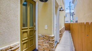 Un callejón estrecho con una valla de madera, un muro de piedra y una puerta amarilla con un ventanal.