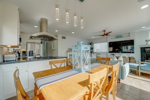 Une cuisine moderne avec un coin repas, comprenant une table en bois, des chaises, des luminaires suspendus et un ventilateur de plafond.
