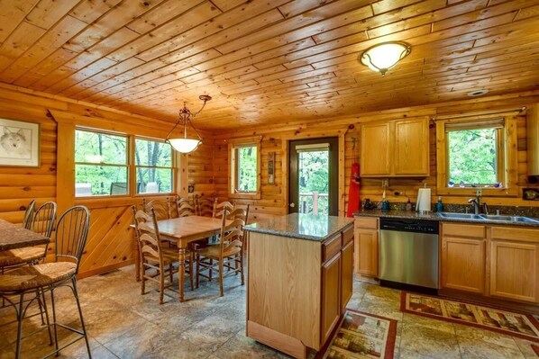 A wooden cabin interior with a dining area, kitchen, and large windows. - Home Sweet Log (Wisconsin Dells)