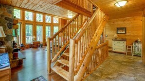 A wooden interior with a staircase, large windows, and a stone wall. - Home Sweet Log (Wisconsin Dells)