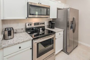 Compact kitchen with modern appliances, oven, stovetop, and refrigerator.