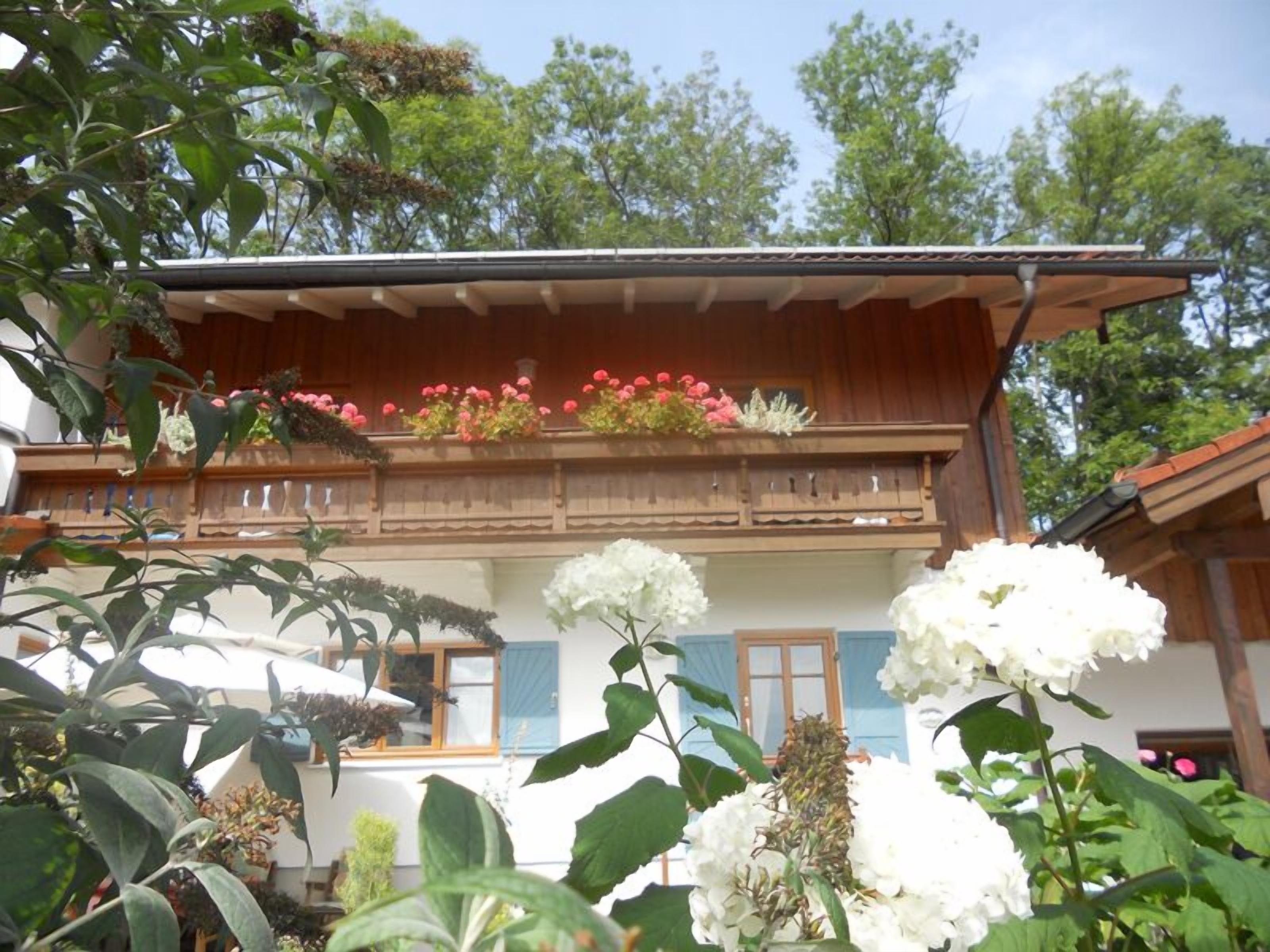 Una cabaña tradicional con balcón de madera decorado con flores, rodeada de abundante vegetación.