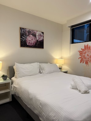 A neatly made bed with white linens, a wall-mounted artwork of flowers, a bedside lamp, and a window with a view. - City-View Chic on Bourke | Free Tram + Netflix (Melbourne)