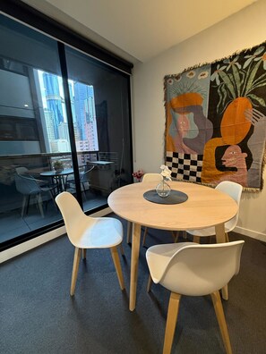 A modern room with a round table, white chairs, a glass wall with a city view, and a large abstract painting on the wall.