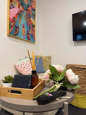 A living room with a TV, a remote control, a decorative box, a potted plant, and a painting on the wall.