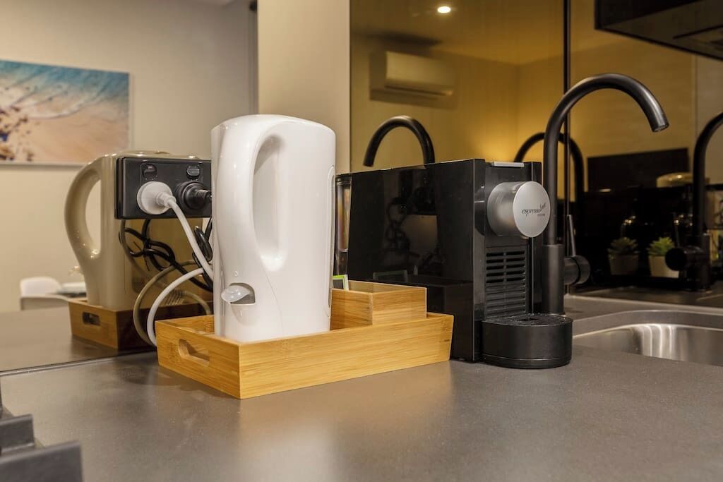 A modern kitchen with a coffee machine, a kettle, and a sink.