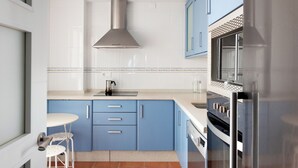 Una cocina compacta con armarios azules, una campana extractora de acero inoxidable y un horno empotrado.