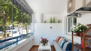 Un balcón con una mesa blanca, un banco acolchado y una planta en maceta.
