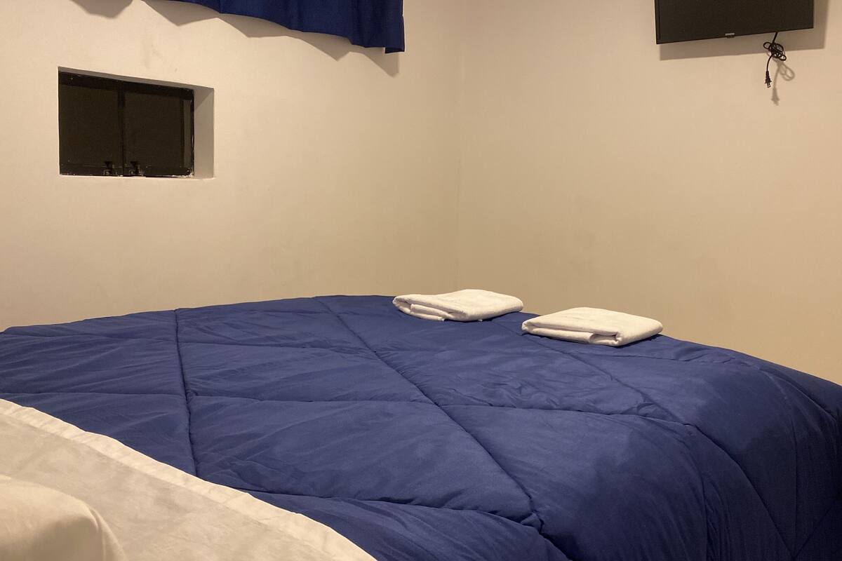 A room with a bed, two towels, a window, and a wall-mounted TV.