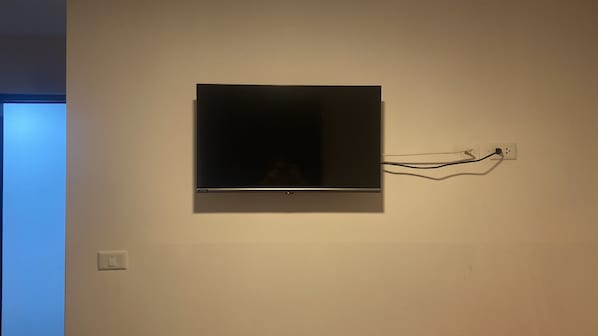 Un televisor montado en una pared lisa, con un enchufe y un interruptor visibles.