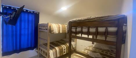 A room with two bunk beds, a blue curtain, and a small table with a lamp.