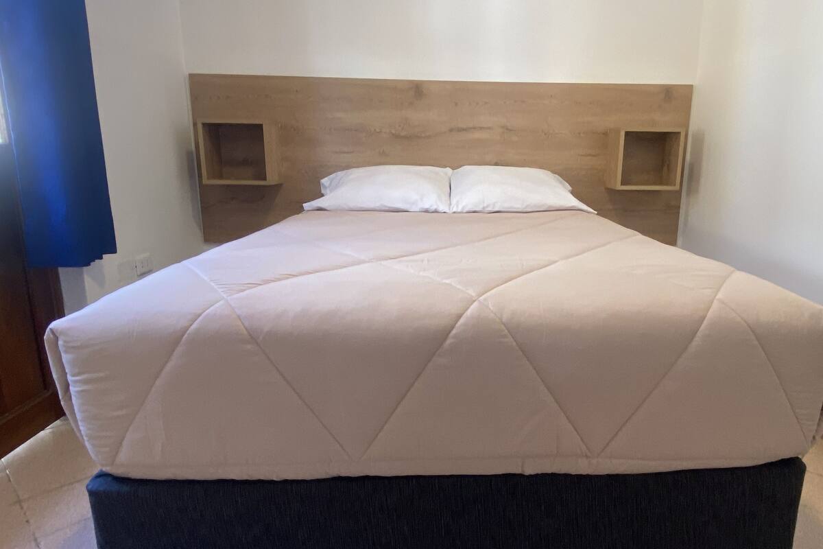 A bed with a wooden headboard, two bedside tables, and a dark-colored skirted bench.
