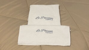 A bed with a beige comforter and two folded white towels with embroidered text. - Hospedaje La Pascana (Cajamarca)
