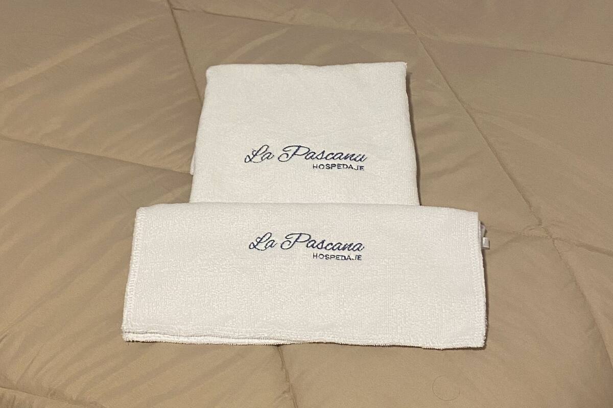 A bed with a beige comforter and two folded white towels with embroidered text.