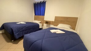Dos camas individuales con ropa de cama azul, almohadas blancas y toallas dobladas.