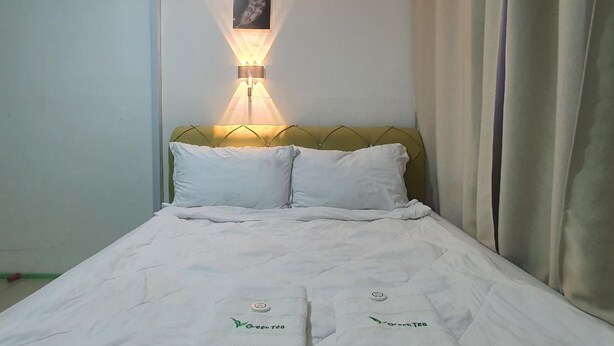 A hotel room with a bed, a wall-mounted air conditioner, a wall-mounted lamp, and a framed picture on the wall.