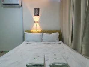 Una habitación de hotel con una cama, aire acondicionado de pared, lámpara de pared y un cuadro en la pared.