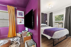 Una stanza con un letto, una TV a schermo piatto, una finestra con tende e un quadro appeso al muro.