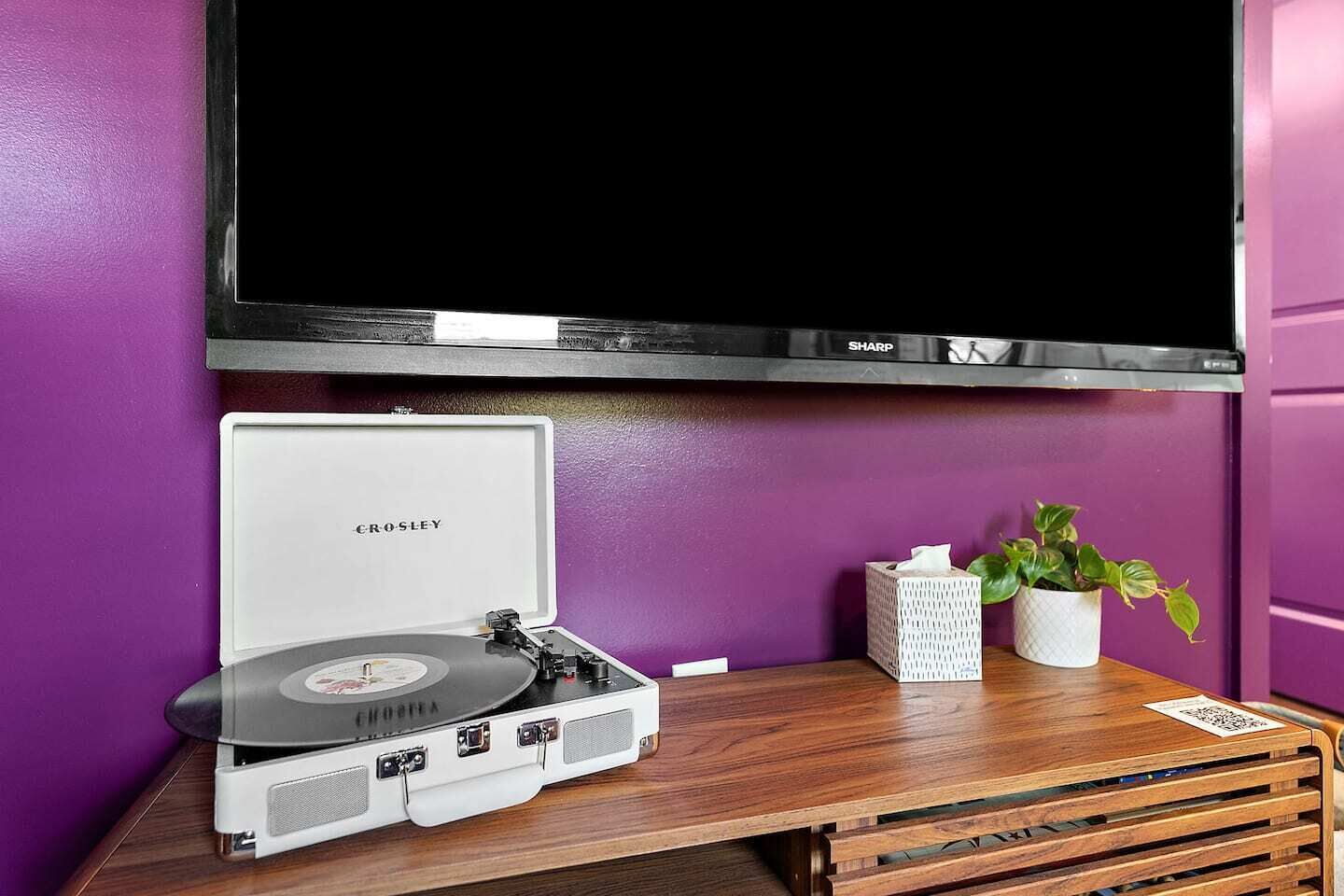 A Crosley turntable on a wooden table with a television above it.