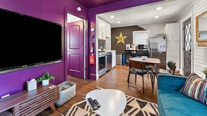 A modern living room with a flat-screen TV, a sofa, a coffee table, and a dining area with a star wall decoration.
