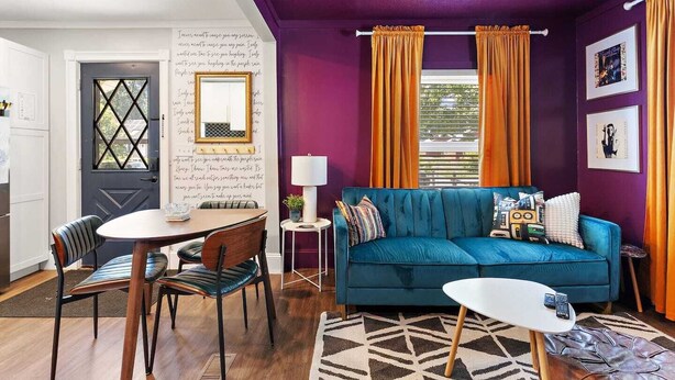 A living room with a blue sofa, a dining table with chairs, a small side table, and a patterned rug.